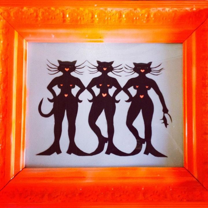 Tre sorte kattedamer med hale og hjerte på brystet står side om side i en selvlysende orange ramme.